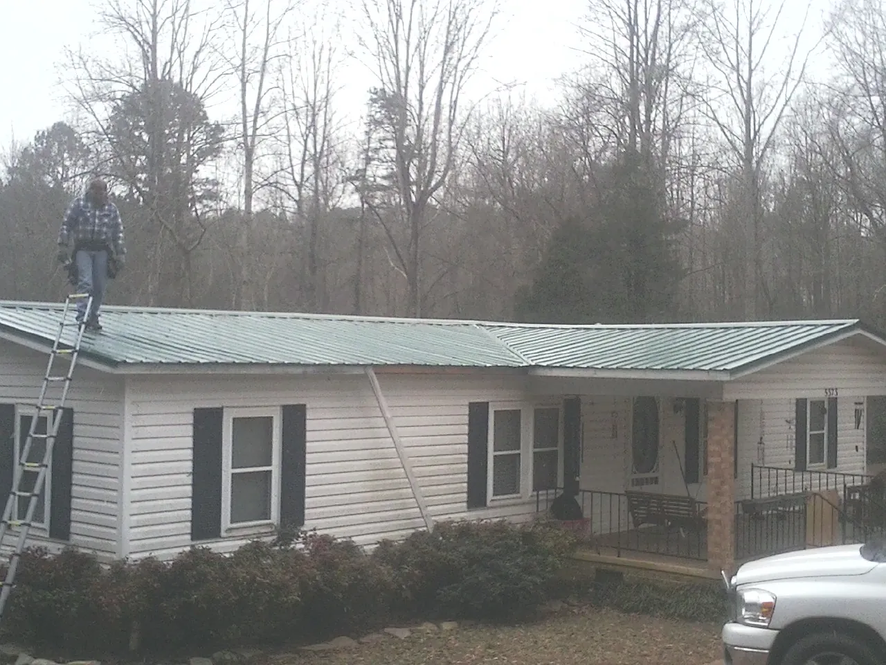 Worker on a ladder beside a new green metal roof on a ranch home in Charleston