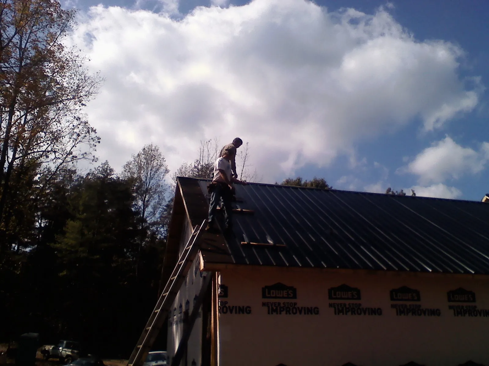 Roofer fastening dark metal panels high against a cloudy sky, from a Roof Inspection job in Charleston